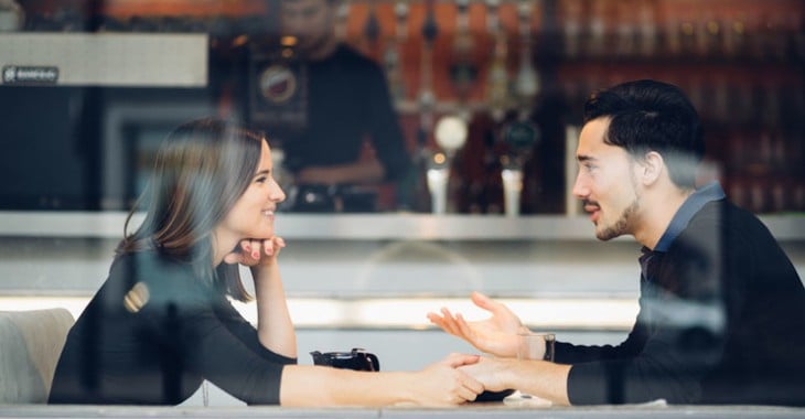 A man and a woman sitting at a restaurant table chatting hand in hand 