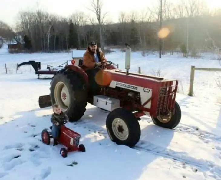 A father with his son each on a tractor in the snow 