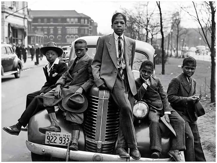 COLORED CHILDREN DRESSED IN SUITS ON TOP OF A CAR