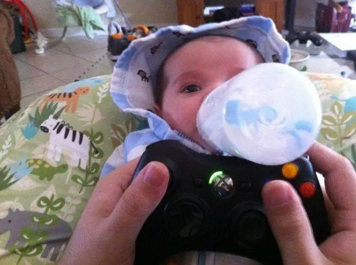 Dad plays Xbox while bottle feeding his son with the controller