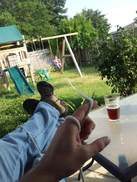 Father pulls son with a string while he's drinking a beer from the shade