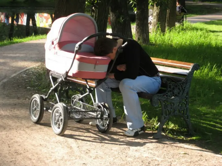 Man asleep on his baby's stroller in a park 
