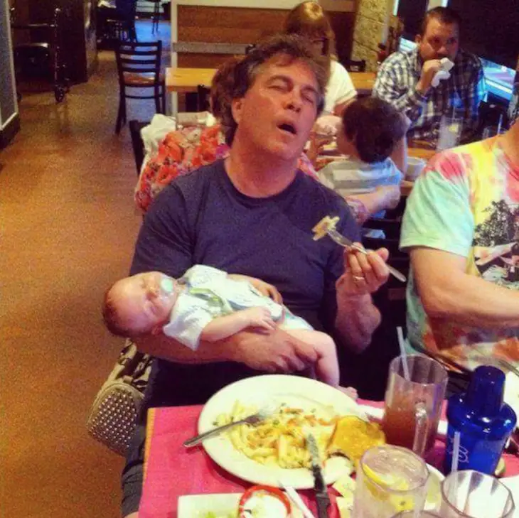 Man asleep with his child in his arms while eating in a restaurant 