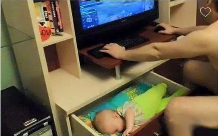 Man at computer with his sleeping baby inside a drawer 