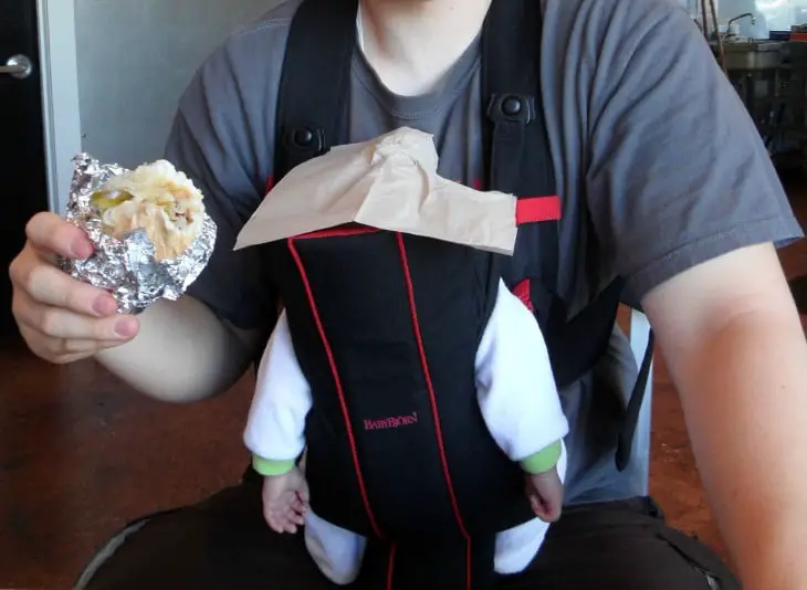 Man eating over his baby's head while carrying him in a fanny pack 