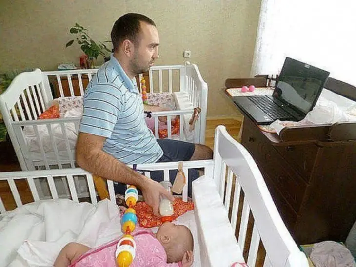 Man feeding his two babies each in their crib 