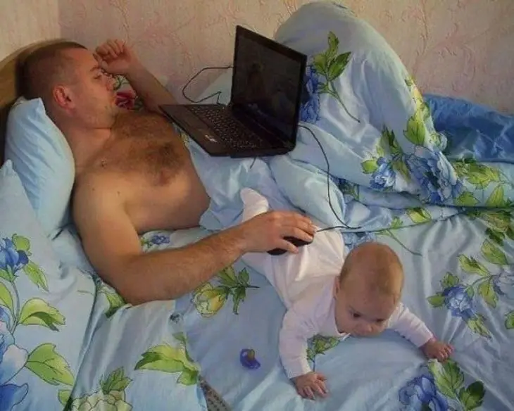 Man lying on computer using his baby to place mouse 