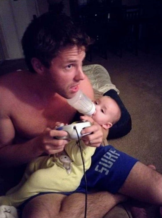 Man playing with his video game and giving bottle to his baby 