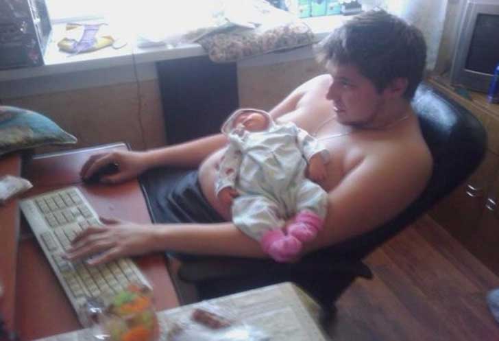 Man sitting in front of a computer with his daughter on his stomach 