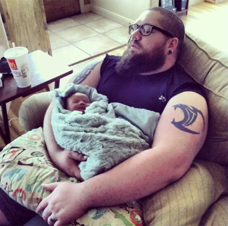Man sitting on a sleeping couch with his baby in his arms 
