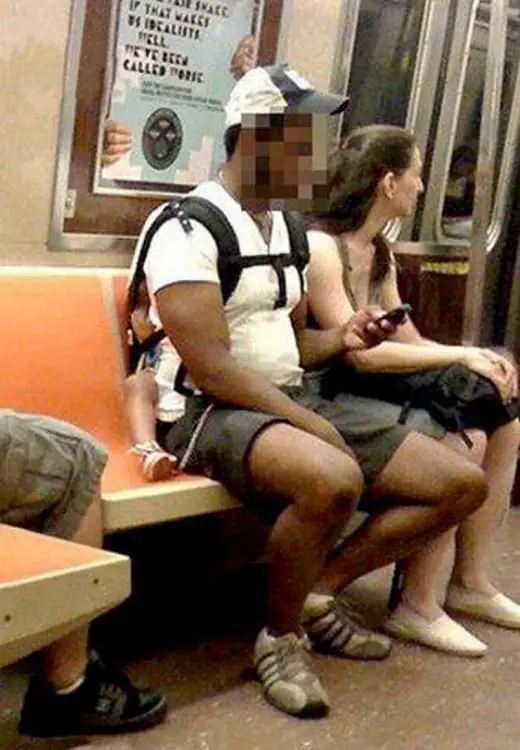 Man sitting on public transport carrying his baby on his back 