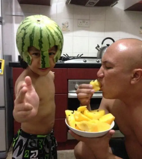 Papa eats pineapple while son poses with watermelon helmet