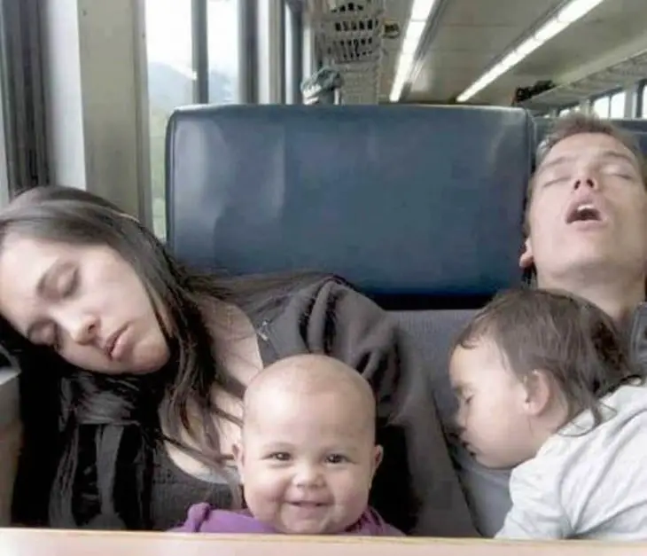 Photograph of two parents asleep with their daughters on a bus 