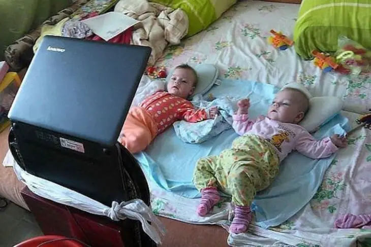 Two babies lying on the bed watching the computer 