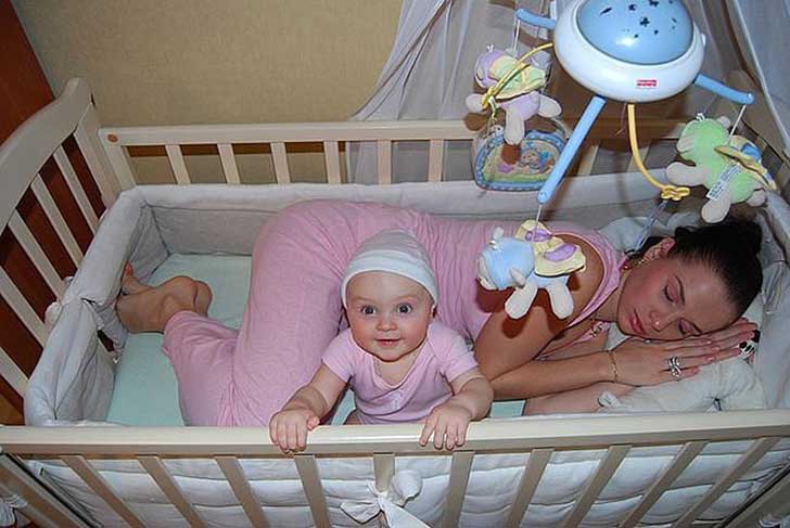 Woman asleep next to her baby on her crib 
