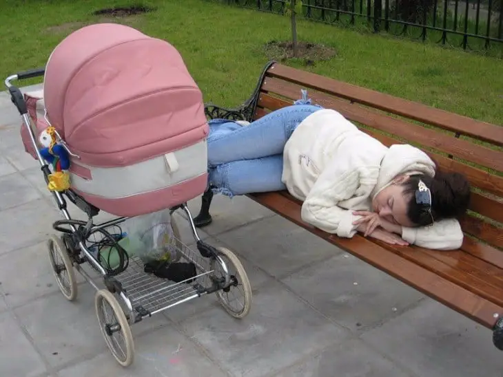 Woman asleep on a park bench next to her baby's stroller 